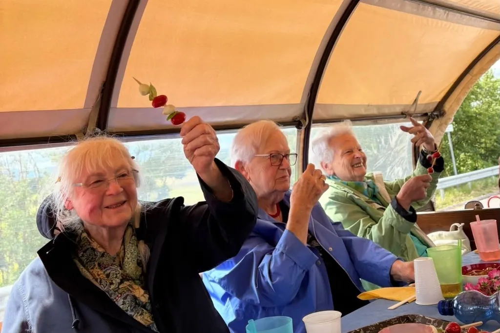Drei fröhliche Seniorinnen und Senioren bei einem Ausflug, die lachend ihre Spieße in die Höhe halten