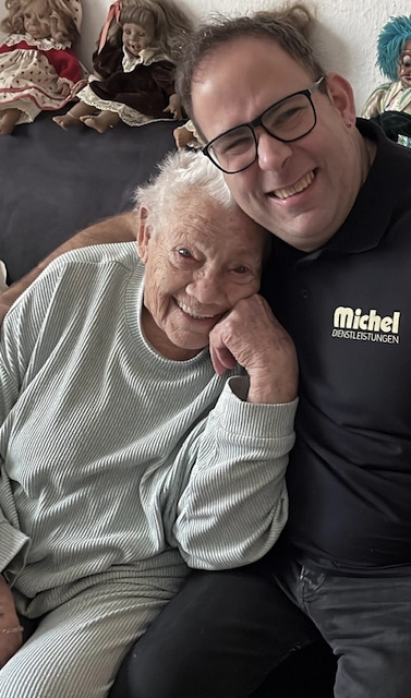 Ein Mitarbeiter von Michel Dienstleistungen Arm in Arm mit einer Seniorin